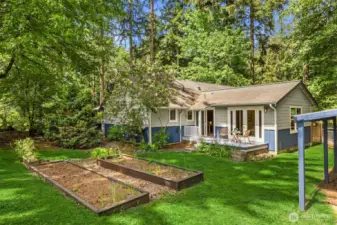 View of part of the backyard with vegetable beds, lawn and a deck with french doors to the primary suite.