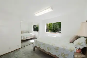 The two additional bedrooms are thoughtfully located at the opposite end of the house from the primary suite, offering privacy and tranquility. In this room, a nice-sized window invites natural light and connects the room to the surrounding beauty, while mirrored double closet doors provide ample storage space as well as enhancing the natural light.