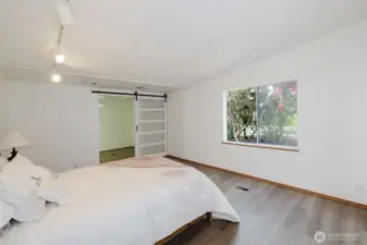 The large primary bedroom boasts beautiful wood laminate flooring and a spacious walk-in closet, highlighted by a stylish barn door with frosted glass panels for added privacy and character.