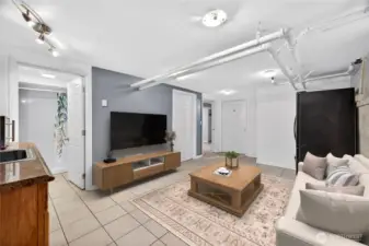 Basement living area viewed from the stairs, with kitchenette, ¾ bathroom, utility room, and access to two bedrooms plus a second refrigerator. (Virtually Staged.)