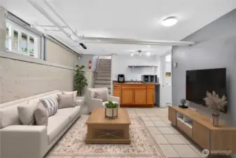 Basement living area from a different perspective, showing the kitchenette, stairs, and ¾ bathroom. (Virtually Staged.)