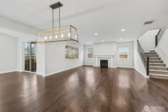 The open living room features a cozy gas fireplace, expansive windows, recessed lighting, and convenient access to the upstairs, blending style and functionality seamlessly.