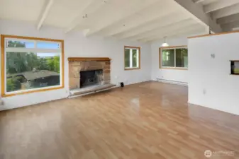 Enter into the living room, with vaulted wood-beamed ceilings and original mid-century stone fireplace. The dining area is in the far corner, and the wall to the right is the open kitchen.