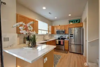 View of kitchen from dining area with stainless appliances and quartz countertops