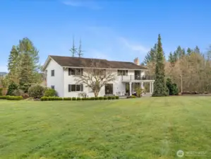 Rear exterior showcasing the home’s scale, large lawn, and elevated deck overlooking the private setting.