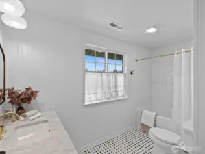 Primary bathroom with tub and tiled shower surround, featuring a window for natural light and a clean, functional layout.