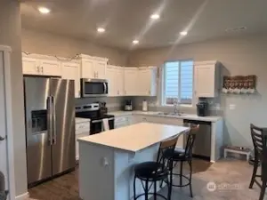 Kitchen features Stainless steel appliances, island, & white cabinetry.