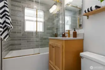 Stylishly updated full bathroom featuring a tiled shower-tub combo with glass doors and modern finishes.