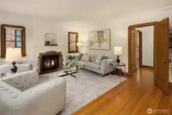 Entry opening to a warm living room with oak floors, mahogany millwork, coved ceilings & fireplace (fire added for visual aid, buyer to verify functionality).