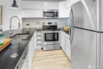 Open kitchen with black quartz countertops and modern updated white cabinets.