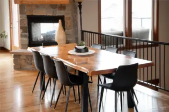 View of dining room w/ double sided stone fireplace, oversized windows and French doors leading out to the main level lake view deck and outdoor living area.