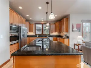 View of main level entertainer's kitchen w/ custom wood cabinetry, stainless steel appliances, granite countertops, and large island w/ bonus prep sink.
