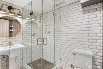 Stylish lower-level ¾ bath with frameless glass shower, subway tile surround, pedestal sink, and modern lighting—fresh, functional, and thoughtfully designed.