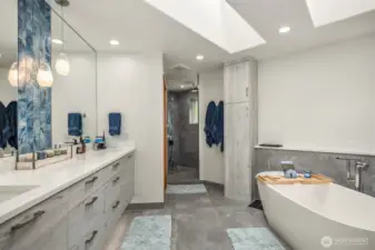 A lavish, stunning, 5-piece en suite bath boasting heated floors, soaking tub, floating dual vanity, large pass-through shower with rain head, bench, and beautiful tilework, fixtures & lighting.