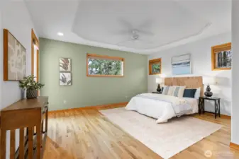 Light pours into the primary bedroom with hardwood floors and tall ceilings.