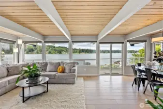 Let the lake greet you every morning. This bright, open living space is wrapped in glass, offering unobstructed views of the shimmering water just beyond. Soft natural light and a warm wood-plank ceiling invite slow mornings and golden-hour gatherings.