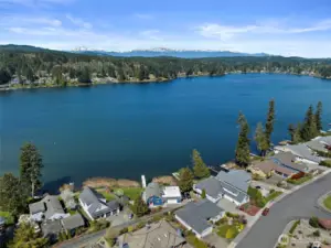 A majestic view from above the lake, revealing forested surroundings and the Olympic Mountains in the distance.