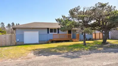 Charming single-level home on a quiet Ocean Park street featuring an attached garage, fresh decking, fenced yard, and a peaceful coastal setting surrounded by mature evergreens.