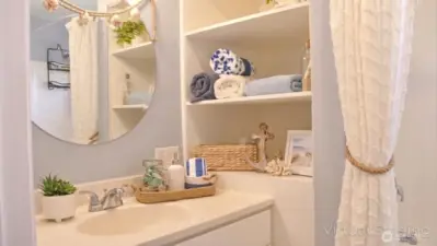 Bright vanity area with open built-in shelving, a clean countertop, and simple coastal touches that add both function and charm.