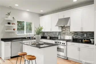 A beautifully appointed kitchen showcases crisp white cabinetry paired with a spacious center island, creating a bright and functional hub for everyday living and entertaining. Sleek black granite countertops provide striking contrast, complemented by the tile backsplash that adds texture and visual interest. The space is outfitted with stainless steel KitchenAid appliances. A walk-in pantry offers abundant storage, enhancing both convenience and organization in this thoughtfully designed kitchen.