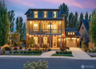 Exterior twilight view of home with classic covered porch, upper view deck and attached 1-car garage.