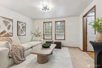 Bright and welcoming sitting room featuring large windows, neutral tones, and a comfortable, modern layout—perfect for gathering or unwinding.