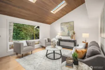 A dramatic vaulted ceiling with warm wood planking and a striking skylight creates an impressive and airy living room filled with natural light. New flooring, fresh paint, and modern furnishings complete this stunning space that sets the tone for the exceptional living experience found throughout this beautifully updated home.