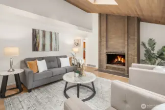 This architecturally distinctive living space showcases a beautiful brick fireplace beneath a vaulted wood-beamed ceiling, creating a warm and inviting atmosphere with genuine character. New flooring and fresh paint throughout elevate the space while honoring its unique mid-century inspired design.