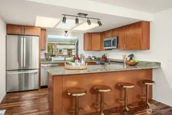 The updated kitchen features rich wood cabinetry, a breakfast bar with seating, and brand-new stainless steel appliances that deliver both style and functionality for the modern home chef. Sleek modern lighting and warm hardwood-style flooring tie the space together beautifully, creating a kitchen that is as inviting as it is practical.