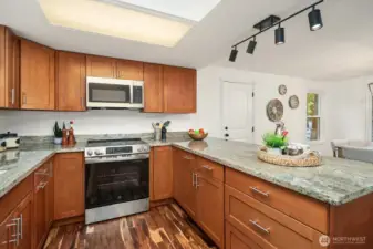 Warm wood cabinetry wraps around this thoughtfully designed kitchen, offering abundant storage and counter space alongside brand-new stainless appliances and granite countertops. Modern track lighting and rich hardwood-style flooring add a polished, contemporary finish to this highly functional and move-in ready space.