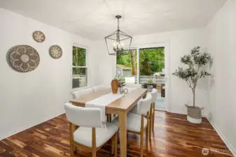 A charming dining area bathed in natural light features rich hardwood flooring, a elegant chandelier, and bright windows that bring the lush outdoor greenery inside. This warm and inviting space flows naturally from the kitchen, creating a seamless setting for both everyday dining and special gatherings.