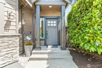 A stylish covered entryway with stone accents, bold columns, and a modern front door creates a warm and inviting first impression!