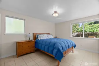 Primary bedroom is roomy and bright with privacy window on the side, and two corner windows opposite, showcasing the gorgeous backyard amenities.  The tile floors have radiant heat throughout, so you always step out of bed to warmth on your toes!