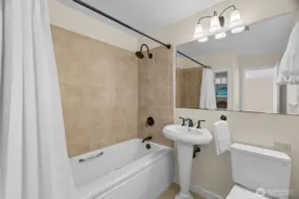 Primary bathroom is fresh and bright as well; tiled shower, large mirror, and built-in storage, with privacy window for natural light.