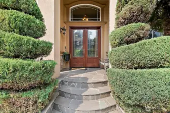 Grand wide stone entryway leads to custom double wood doors.