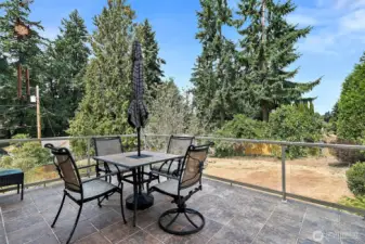 A spacious deck off the kitchen and family room, featuring tile flooring and glass railings.  It offers uninterrupted views perfect for enjoying the outdoors in style.