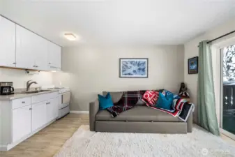 Cozy studio living area featuring a pull-out sofa bed, efficient kitchenette, and LPV flooring throughout. An inviting space that easily transitions from daytime comfort to overnight accommodations, with natural light and balcony access just beyond.