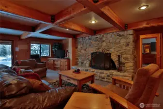 A beautifully crafted lower level lounge  with exposed beams and a dramatic river rock fireplace, embodying true alpine charm