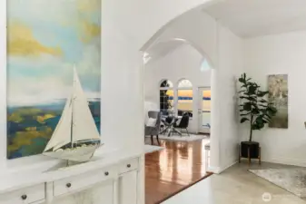 Bright and inviting entry with arched detailing, hardwood floors, and a serene coastal aesthetic leading to open-concept living with water views.