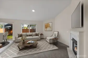 Spacious and bright living area featuring vaulted ceilings, a cozy tiled gas fireplace, and large windows that bring in abundant natural light with a view of the backyard. Perfect for relaxing or entertaining.