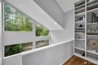 Stepping out to the cozy loft where a dramatic floor-to-ceiling bookcase is the perfect spot to enjoy a book while looking out the windows to nature
