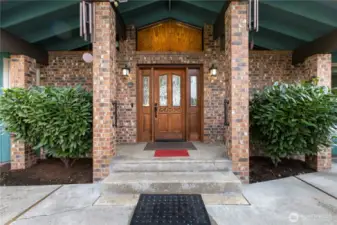 Welcoming covered entry w/stately brick columns leading to a classic wood front door.