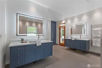 The double vanities have lighted vanity mirrors with defogging features. there is an entrance to the pool patio from the primary bath