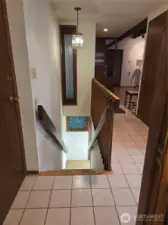 Stairs down to lower level, and view towards the entryway and living room on the right. Garage entery is the door on the left.