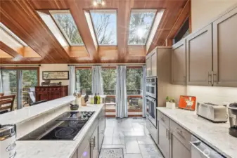 Another view of the kitchen looking toward the back deck with the cooktop on the left and the microwave, oven and dishwasher on the right. Note the ceramic tile floors throughout the kitchen space.