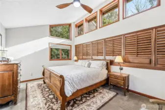 The primary bedroom is on the upper level. This room features vaulted ceilings and wood-wrapped windows that bring in light from three sides. The tasteful shutters offer privacy from the rooms below.