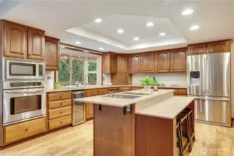 Spacious cook’s kitchen with plentiful cabinetry, center island with seating, stainless appliances, and a big window over the sink that looks out to the trees and deck.