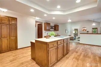 Open kitchen layout with central island, bar seating, and clear sightlines into the family room—so the cook can stay connected to homework time, game day, or guests while prepping meals.