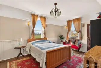 The main floor primary bedroom is a bright, airy retreat. It has plenty of classic character with those original wood floors and vintage lighting, plus big windows that look right out over the fields to the south and the backyard to the west. Having direct access to a 3/4 bathroom right here on the main level makes it a super convenient and peaceful spot to start your day.