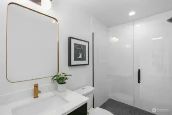 This pristine bathroom sports a spacious walk-in shower, vanity with quartz counters and subtle gold hardware accents for an elevated look.